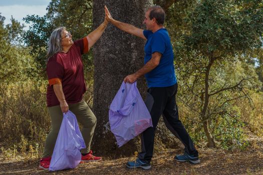 environmentalist couple high-fiving in the bush cleanup with garbage bags in their hands.