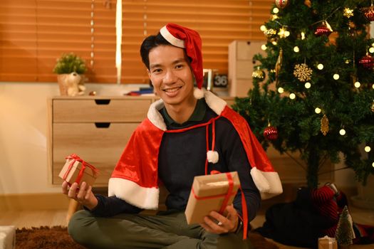 Handsome man in Santa hat holding Christmas gifts and smiling to camera, celebrating New year and Christmas festive.