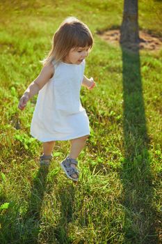 charming child in linen dress walking on the lawn.
