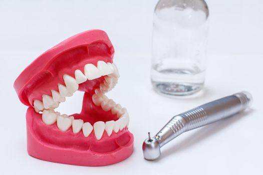 Head of high-speed dental handpiece with bur and a layout of the human jaw with a glass of water on the white background. Dental instruments for dental treatment. Close-up view.