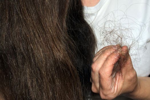 A girl with long dark hair holds a bunch of fallen hair in her hand. Hair loss problem.