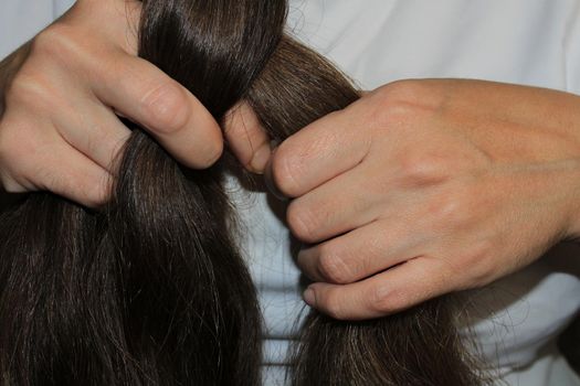 A girl with long dark hair is braiding her hair. Close-up hands. Hair care. Hair loss problem.