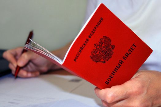 The girl holds a military ID issued by the Russian Federation in her hand and writes down his data. The concept of mobilization.