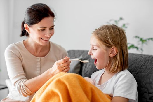 Mother gives ill sick child daughter medicine syrup at home. Mom woman cares about kid with fever and virus