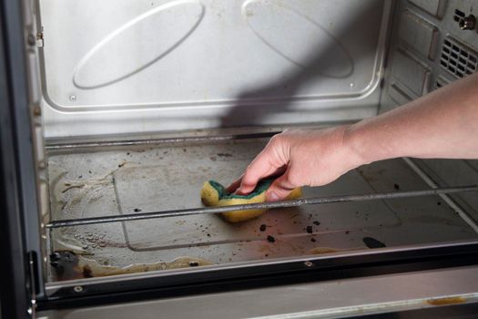 Female hand with sponge and detergent cleaning the kitchen oven from burnt drops, housekeeping concept. Scrubbing the stove, High quality photo