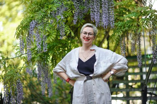 Thoughtful happy mature woman surrounded by chinese wisteria.