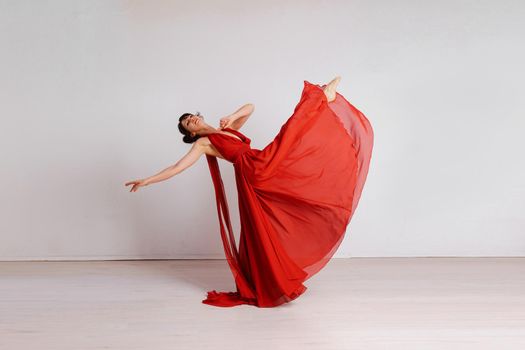 Dancer in a red flying dress. Woman ballerina dancing on a white studio background.