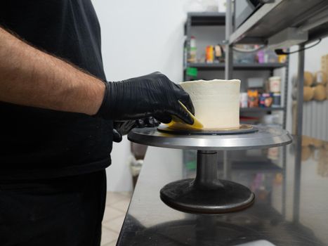 Decorator using spatula and scraper to smooth buttercream on a frosted cake