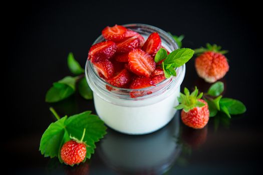 Sweet homemade yogurt with fresh ripe strawberries in a glass jar isolated on black background