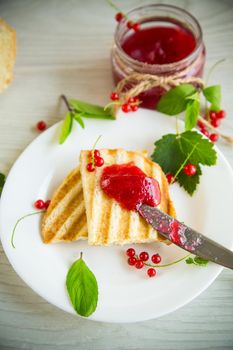 fried bread croutons for breakfast with redcurrant jam in a plate with berries on a wooden table.