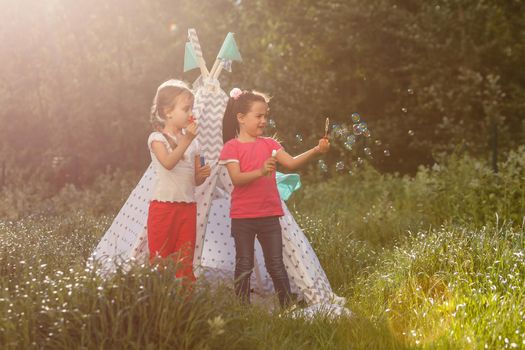 Two happy laughing little girls in camping tent in dandelion field