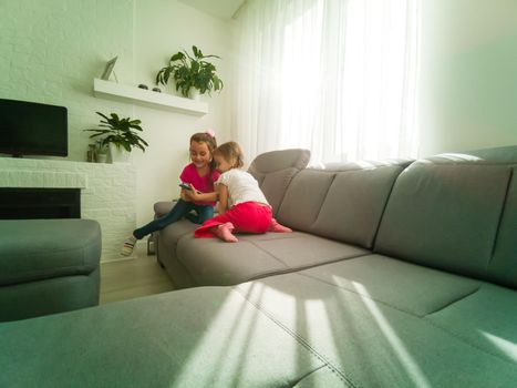 Two kids with gadgets. Sister and brother sharing funny content on smartphone and digital tablet on sofa at home. Family friendship and communication concept