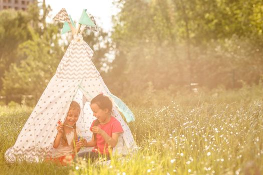 Two happy laughing little girls in camping tent in dandelion field