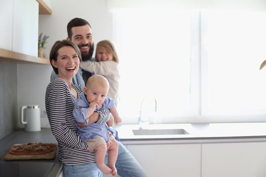 Family of 4 posing in the kitchen smiling and happy