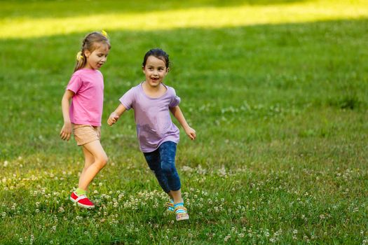 Two sisters running on the lawn in the city park outdoor. Freedom and carefree. Happy childhood