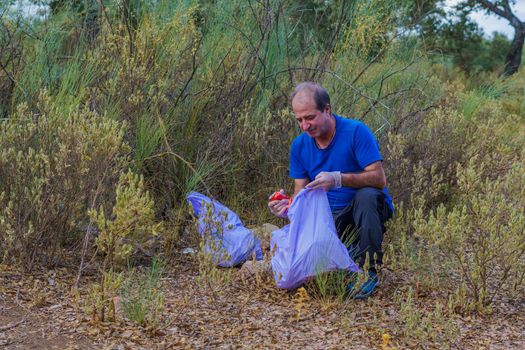 environmentalist man with garbage bags picking up garbage from the field and taking care of the environment