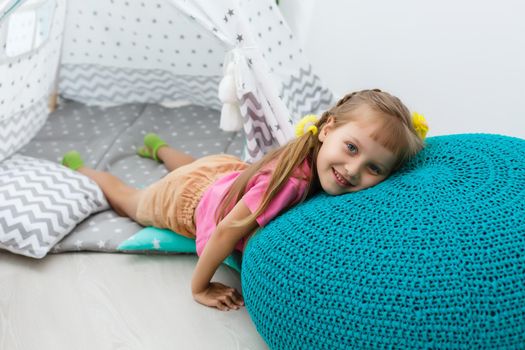 little girl on a children's ottoman near a wigwam