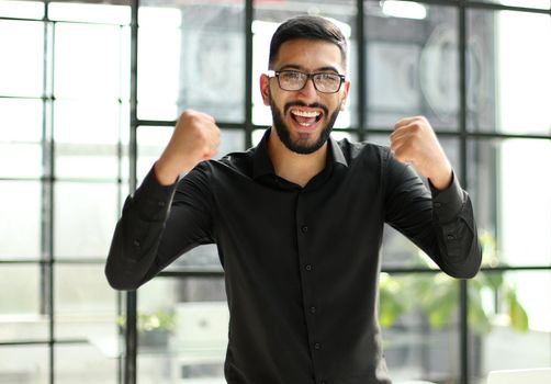 young businessman celebrating success in his home office holding fists up celebrating achievement