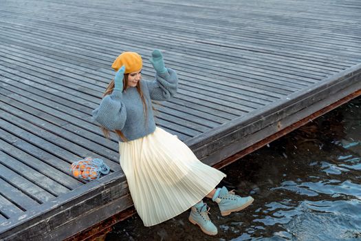 Outdoors fashion portrait of a beautiful middle aged woman walking on the beach. Marine background. Dressed in a stylish warm blue sweater, yellow skirt and beret