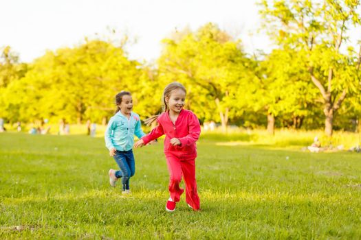 Children run on the green grass holding hands. Girls running around the lawn with grass playing with splashes of water to water plants.