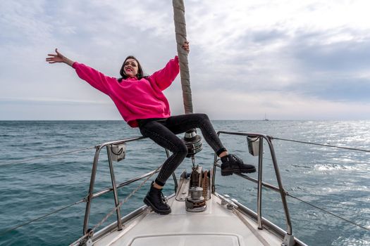 Woman standing on the nose of the yacht at a sunny summer day, breeze developing hair, beautiful sea on background.