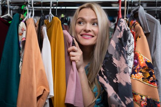 A happy woman shopping. The backstory of a clothing store. A thrilling and exciting shopping experience for every woman. . Blonde woman with straight long hair.