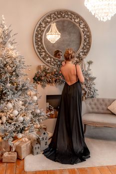 Portrait of a wealthy mature woman with evening make-up and hairstyle posing in a black dress on the background of the Christmas room. Luxurious lifestyle. Christmas holidays concept.