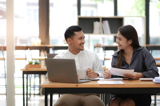 Two employees in a modern office, an Asian man and a woman working at a table, colleagues discussing and consulting, thinking about a joint project.