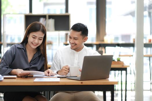 Two employees in a modern office, an Asian man and a woman working at a table, colleagues discussing and consulting, thinking about a joint project.