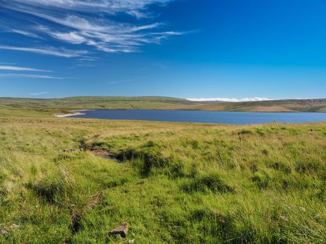 Cow Green Reservoir and dam, on the River Tees, under blue sky and white wispy clouds, North Pennines, UK