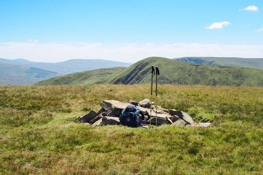 A hiker places down rucksack and walking poles at the summit of Randygill Top with views across the Howgill Fells, Cumbria, UK