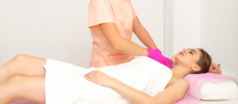 Beautician with a patient during sugaring. The cosmetologist waxes the female armpit