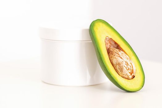 Skincare with natural cosmetics. White cosmetic jar of cream with half of the avocado near against white background, copy space, mockup