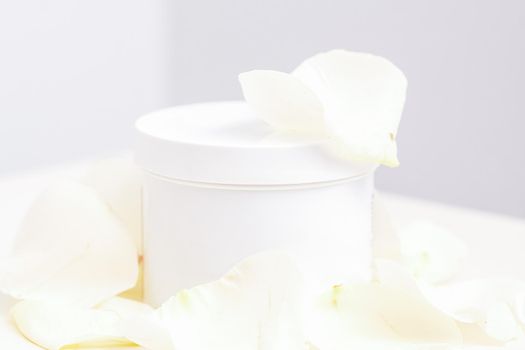 White jar with cream among delicate white rose flowers petals on a light background. Natural organic cosmetics concept, close up, mock-up