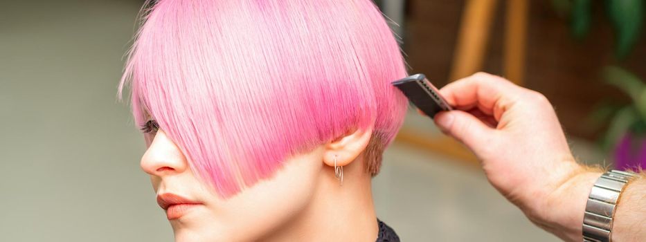 A hairdresser is combing the dyed pink short hair of the female client in a hairdresser salon