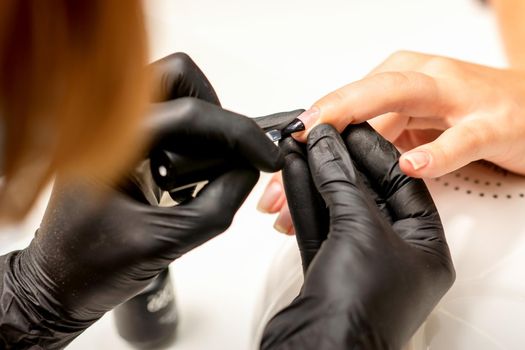 Manicure painting process. Manicure master paint the nails with transparent varnish in a nail salon, close up