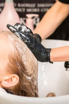 Young caucasian woman with closed eyes getting washing hair by a professional hairdresser in a beauty hair salon