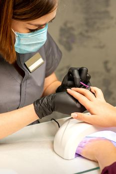 Professional manicure. A manicurist is painting the female nails of a client with purple nail polish in a beauty salon, close up. Beauty industry concept