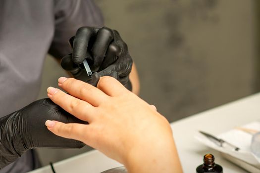 Manicure painting process. Manicure master paint the nails with transparent varnish in a nail salon, close up