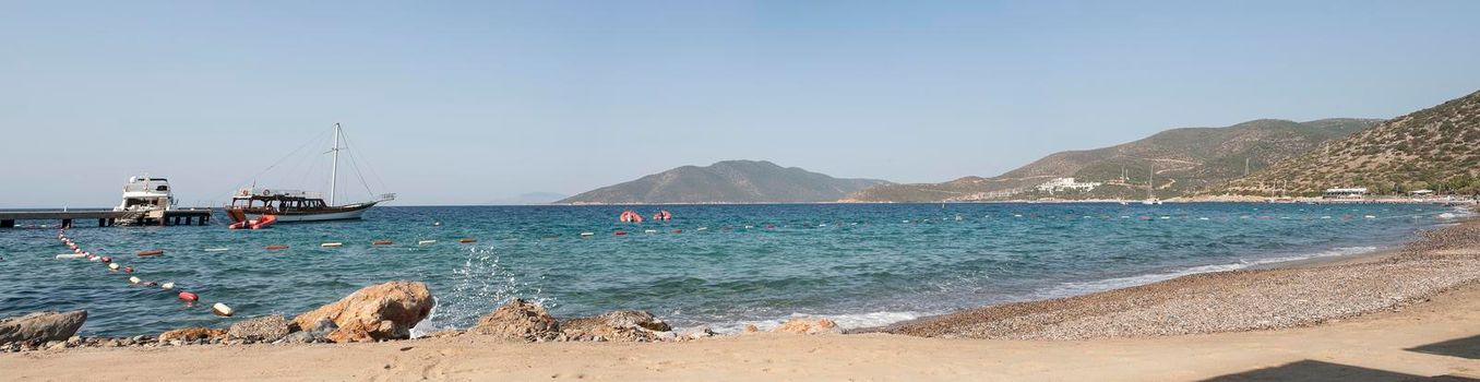 Bodrum - nice view of the sea. Beach Bodrum with sand and mountains, the sea with the ship. Beautiful harbor near the sandy beach.