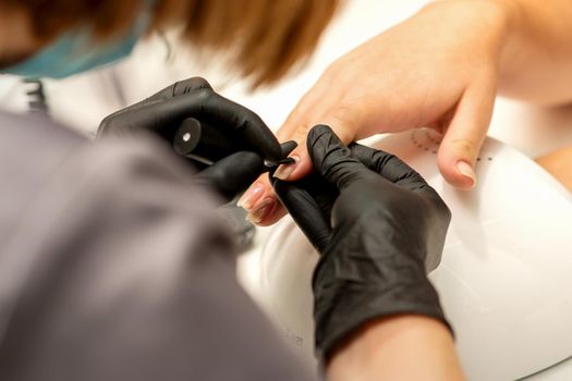 Manicure painting process. Manicure master paint the nails with transparent varnish in a nail salon, close up