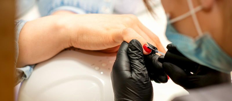 Professional manicure. A manicurist is painting the female nails of a client with red nail polish in a beauty salon, close up. Beauty industry concept