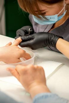 Manicure master removes cuticles from female nails with scissors wearing protective gloves in manicure salon