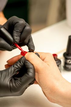 Professional manicure. A manicurist is painting the female nails of a client with red nail polish in a beauty salon, close up. Beauty industry concept