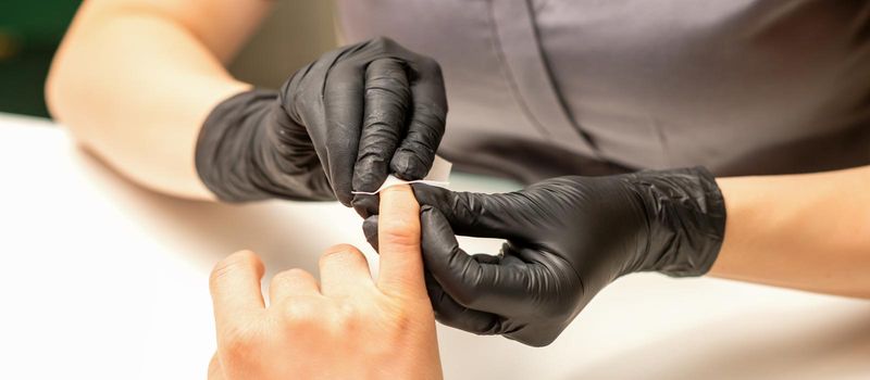 The manicurist finishes the procedure for red nail polishing and cleaning with a cotton napkin, pad, swab in a beauty salon, close up