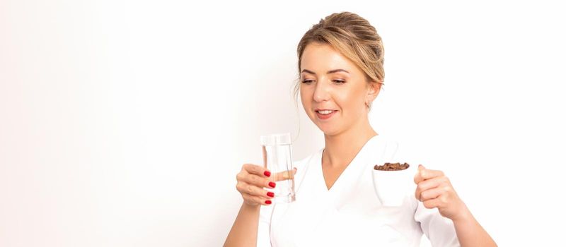 Coffee with water. The female nutritionist holds a cup of coffee beans and a glass of water in her hands on white background