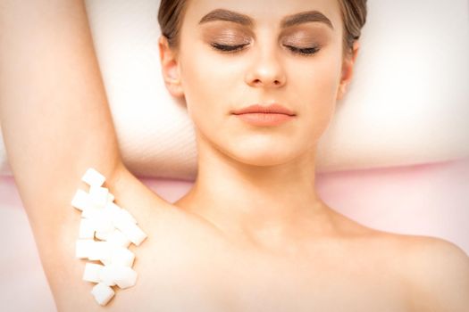 Sugaring, waxing concept. White sugar cubes lie down on the female armpit of the young white woman, close up