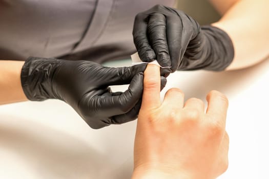 The manicurist finishes the procedure for red nail polishing and cleaning with a cotton napkin, pad, swab in a beauty salon, close up