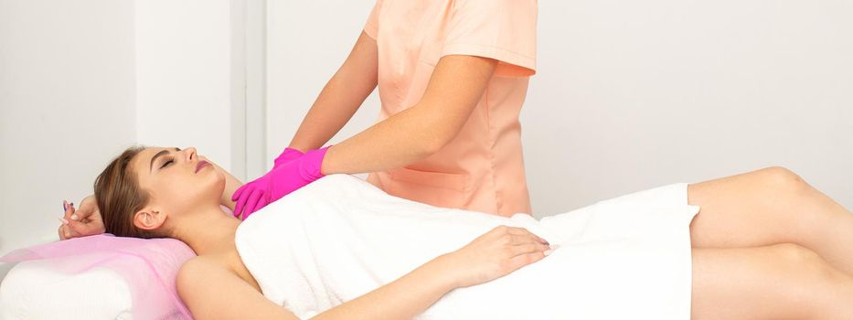 Beautician with a patient during sugaring. The cosmetologist waxes the female armpit