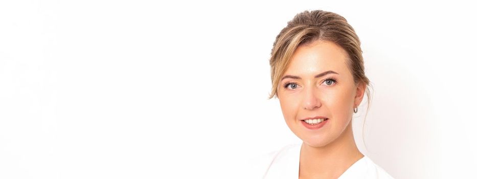 Close-up portrait of young smiling female caucasian healthcare worker standing staring at the camera on white background